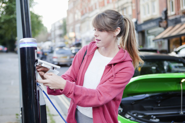 Woman charging electric car on street © Nancy Honey/Cultura/Getty Images