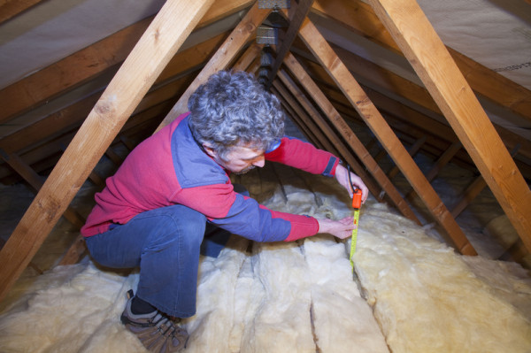 Man measuring the depth of insulation in a house loft or roof space
