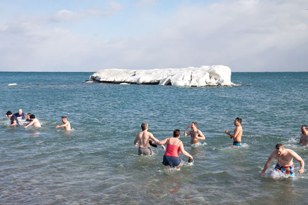 people entering water with frozen rock in background