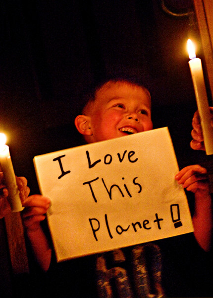 A young boy holding up a handmade sign reading "I love this planet!" in a candlelit room during Earth Hour 2010, Canada. © Jeremiah Armstrong / WWF-Canada