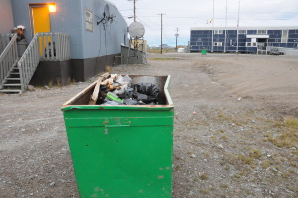 Garbage sits in an open bin on the street. This is an invitation to Polar bears (Ursus maritimus) who are hungry at this time of the year and are forced to wait longer for the ice to form so they can go out to hunt. Resolutions are sought to these conflicts between humans and polar bears. Arviat, Nunavut, Canada