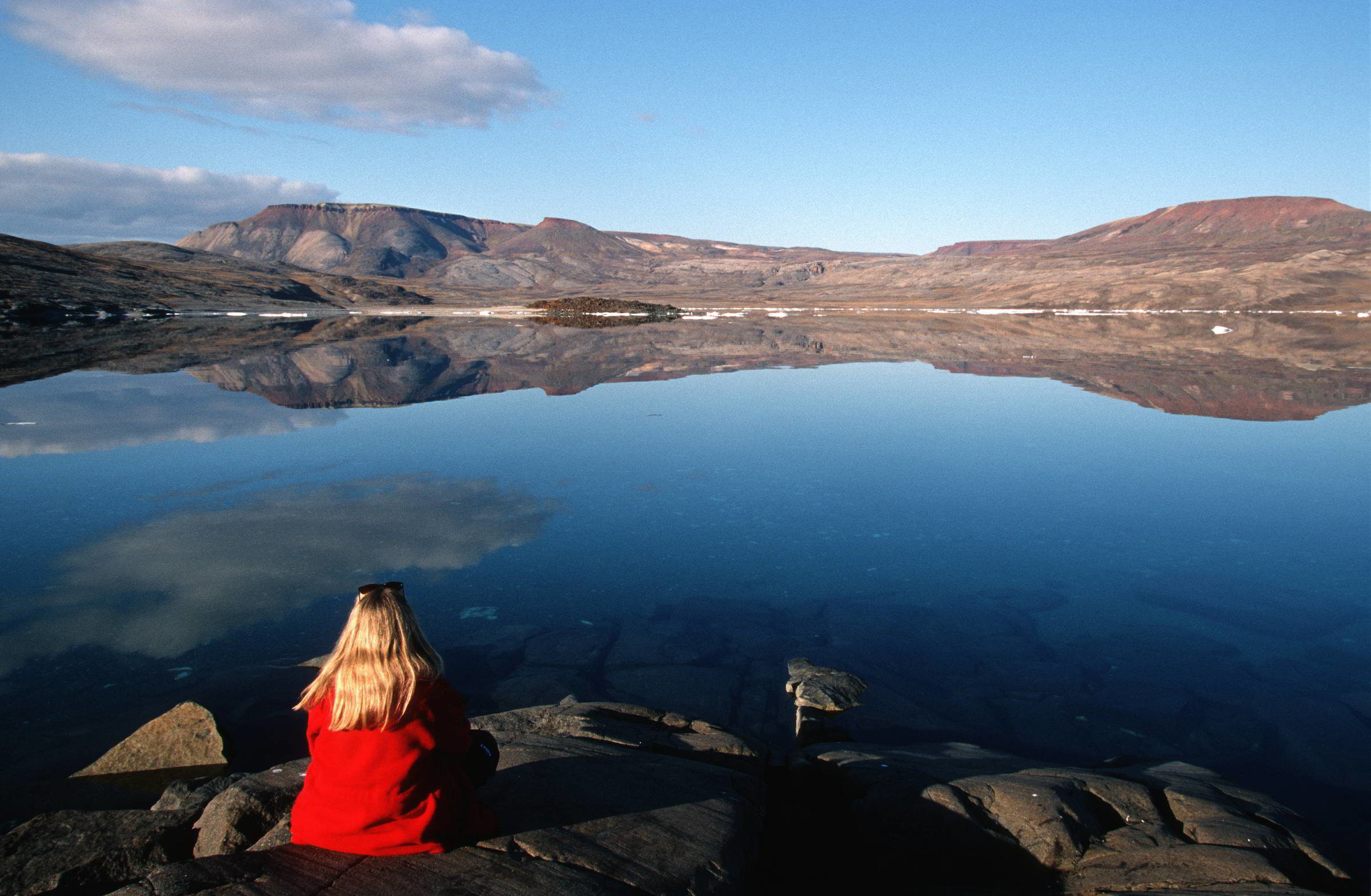 Woman sits on the rocky shore of Victor Bay on north Baffin Island, Nunavut, Canada