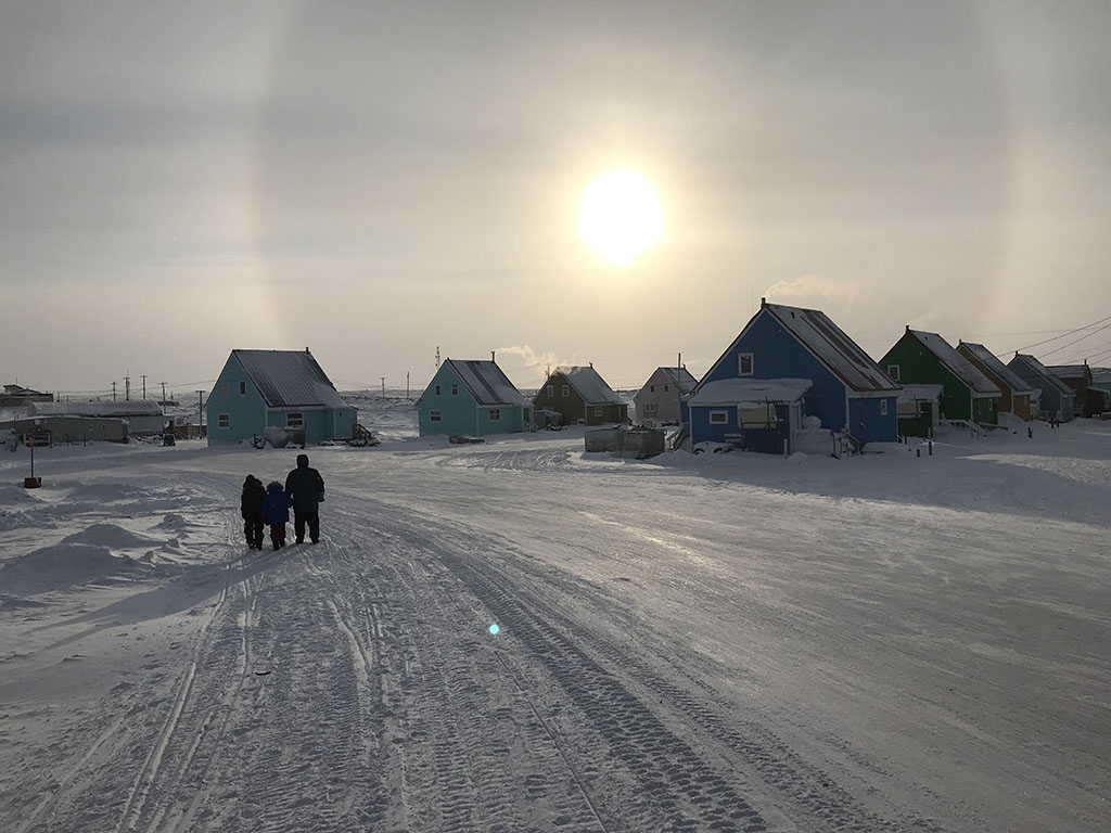 Deux résidents inuits de Taloyoak, au Nunavut, marchent au soleil, un parhélie dans le ciel.