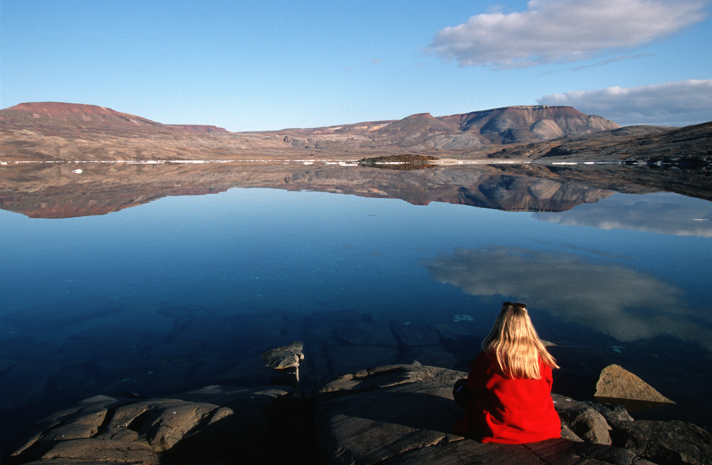Woman sits on the rocky shore of Victor Bay on north Baffin Island, Nunavut, Canada.