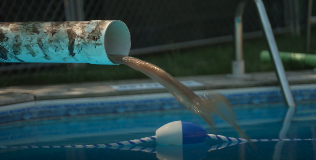 Pipe dumping brown liquid into a swimming pool