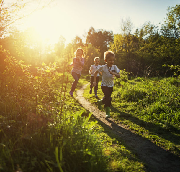 Three children running on a path in a wooded area