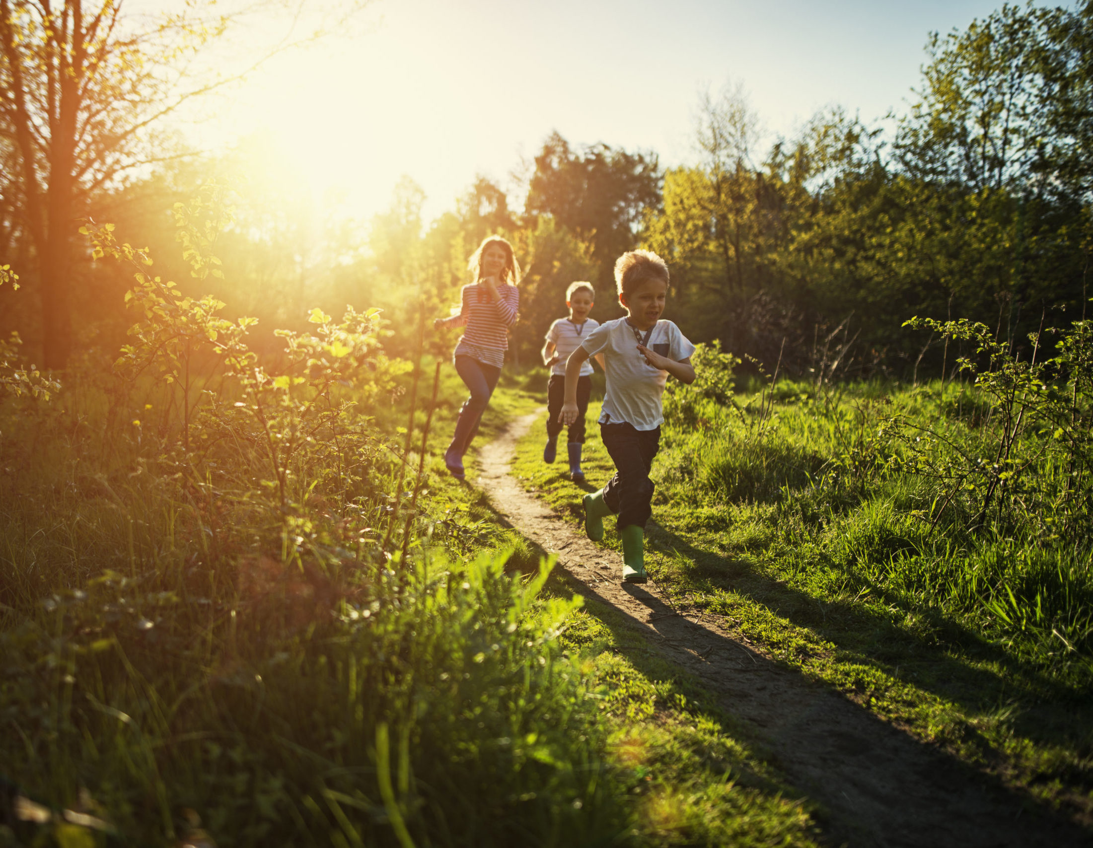 Three children running on a path in a wooded area