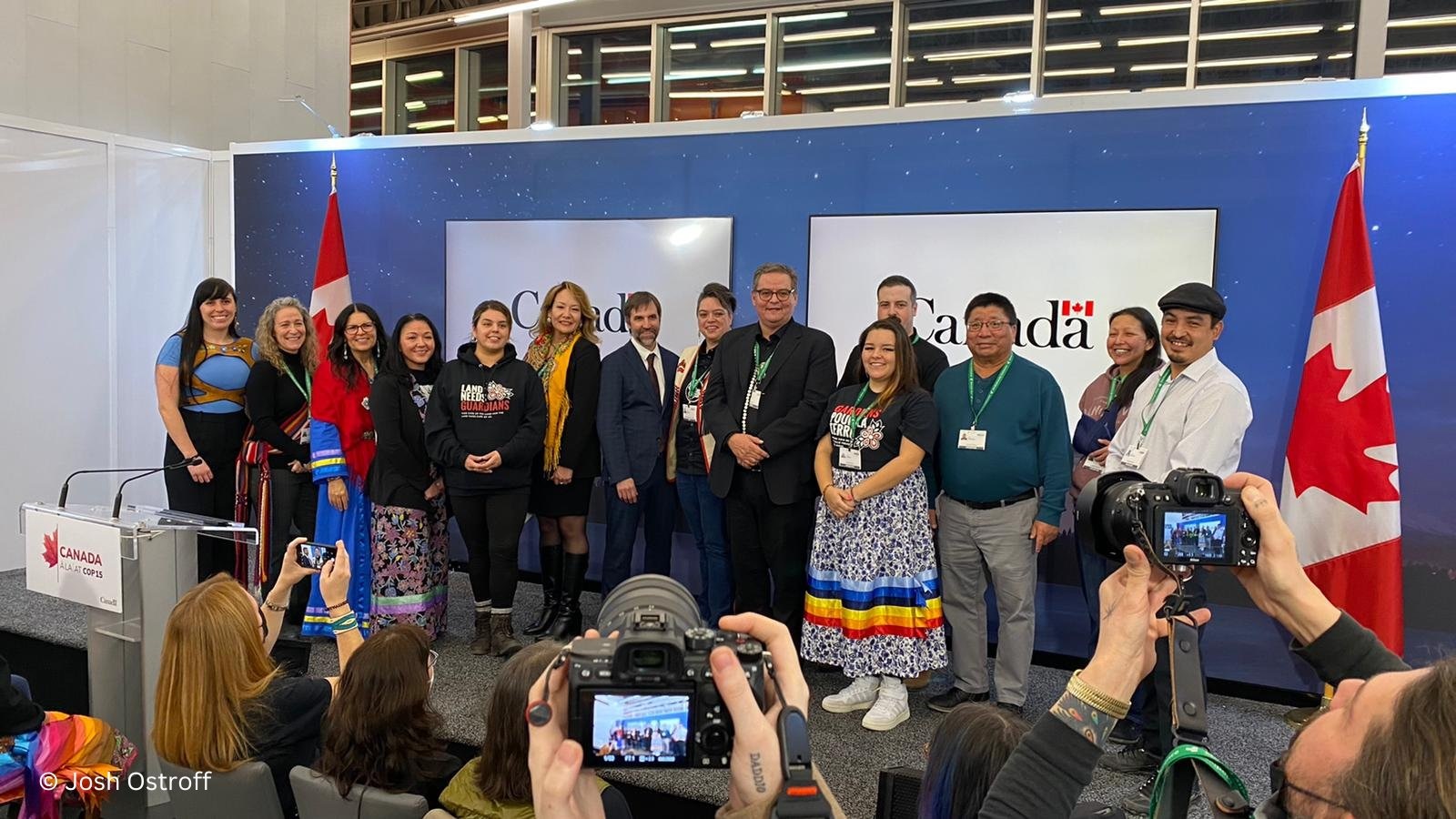 A crowded stage with Indigenous guardians and the environment minister in the middle posing for a group photo