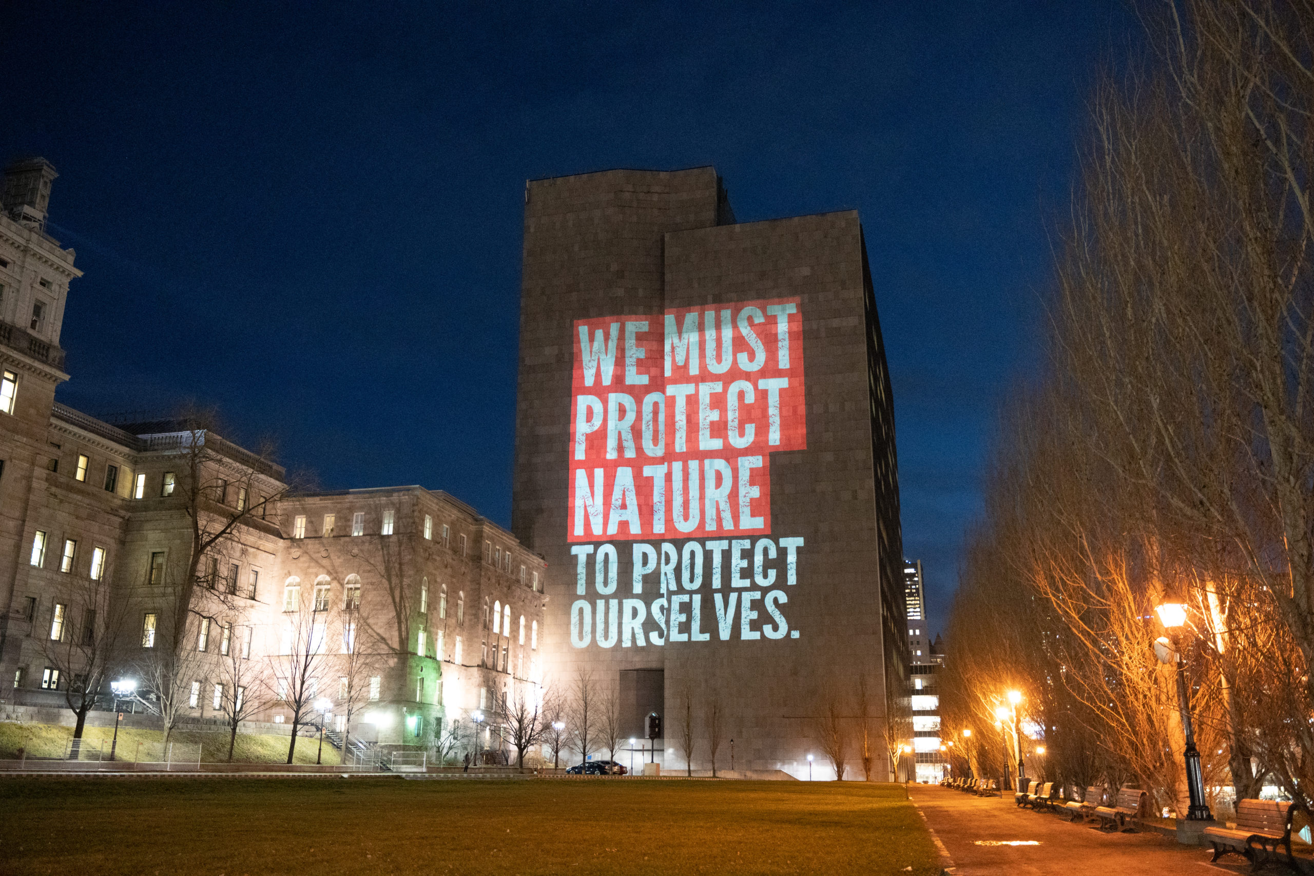 Projection on building wall that reads We must protect nature to protect ourselves
