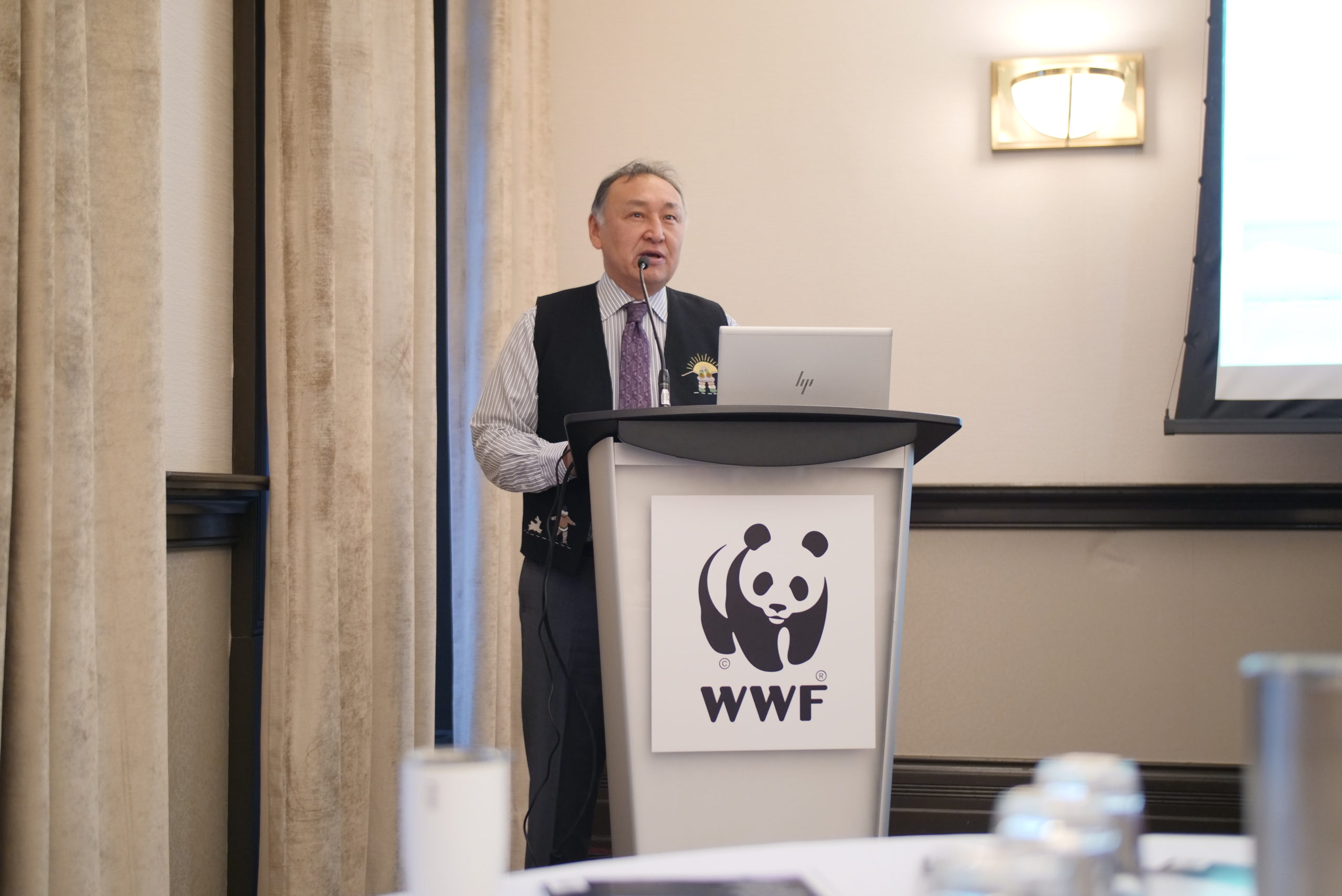 Inuit man standing behind a podium with a WWF panda logo on it