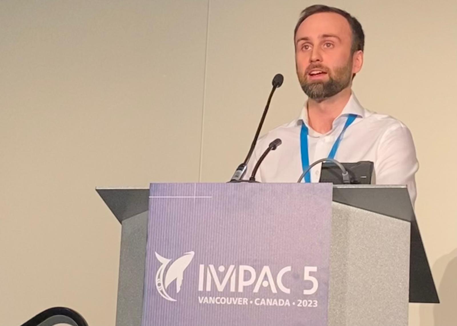 A man standing at a podium with an IMPAC5 sign on it