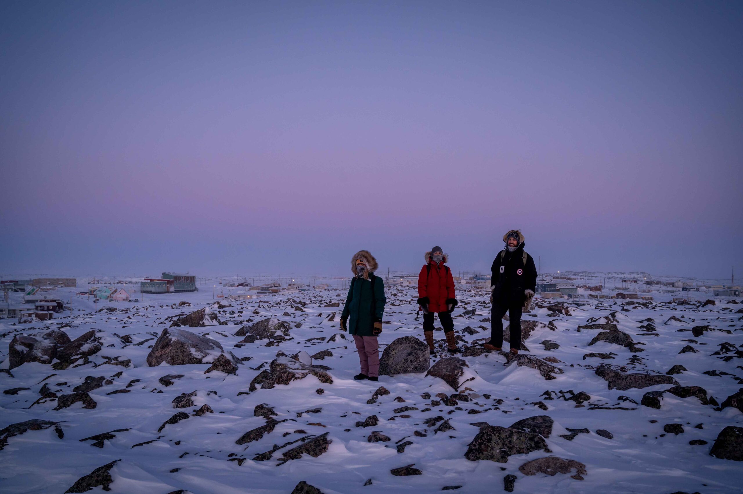 Three people walking on an Arctic landscape during a winter sunset 