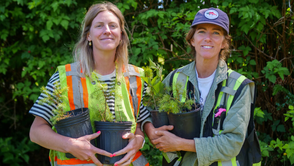 Two women holding plants. Redd Fish Restoration Society’s Mandala Smulders (Director of Operations) and Jessica Hutchinson (Executive Director and Ecologist)