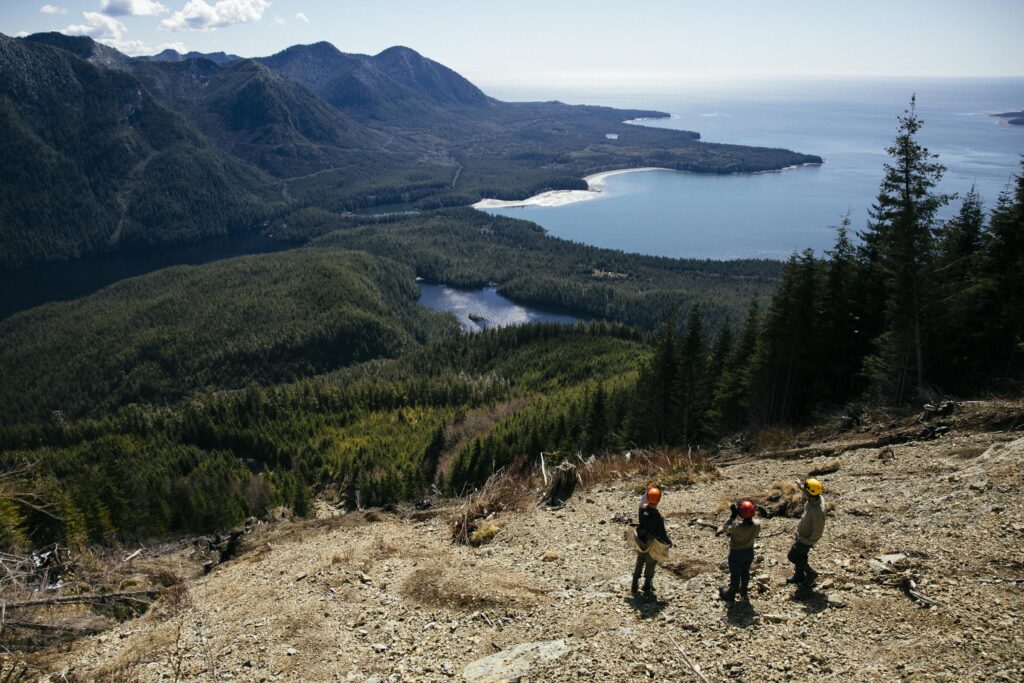 Three people survey erosion damage on a mountain slope in B.C.