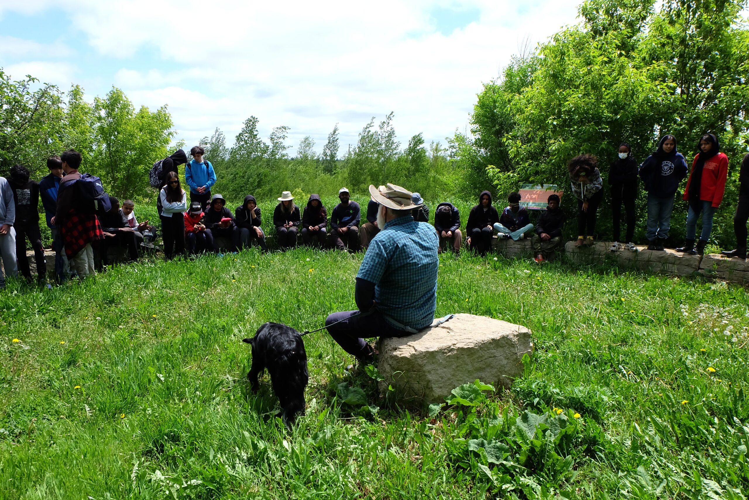 An adult person and a dog seen from behind, with a half circle of  adolescents volunteers in Markham, Ont. 