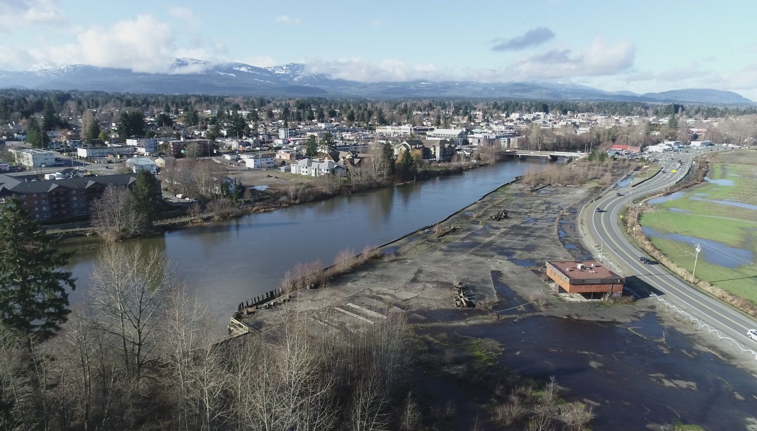 An aerial photo of a river near a former industrial site, with houses and mountains in the background in Courtenay, B.C. 