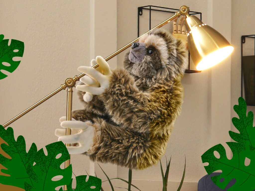 A plush sloth with velcro hands hangs onto a lamp like a tree.