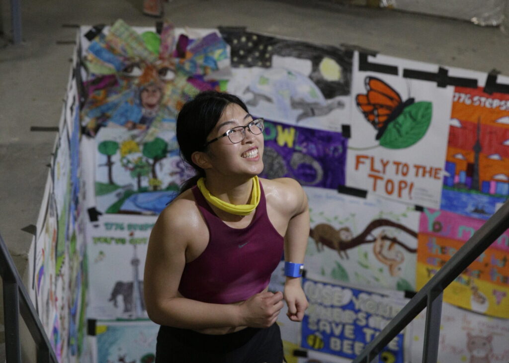 A young women jogs to the top of the stairwell with children's artwork in the background.