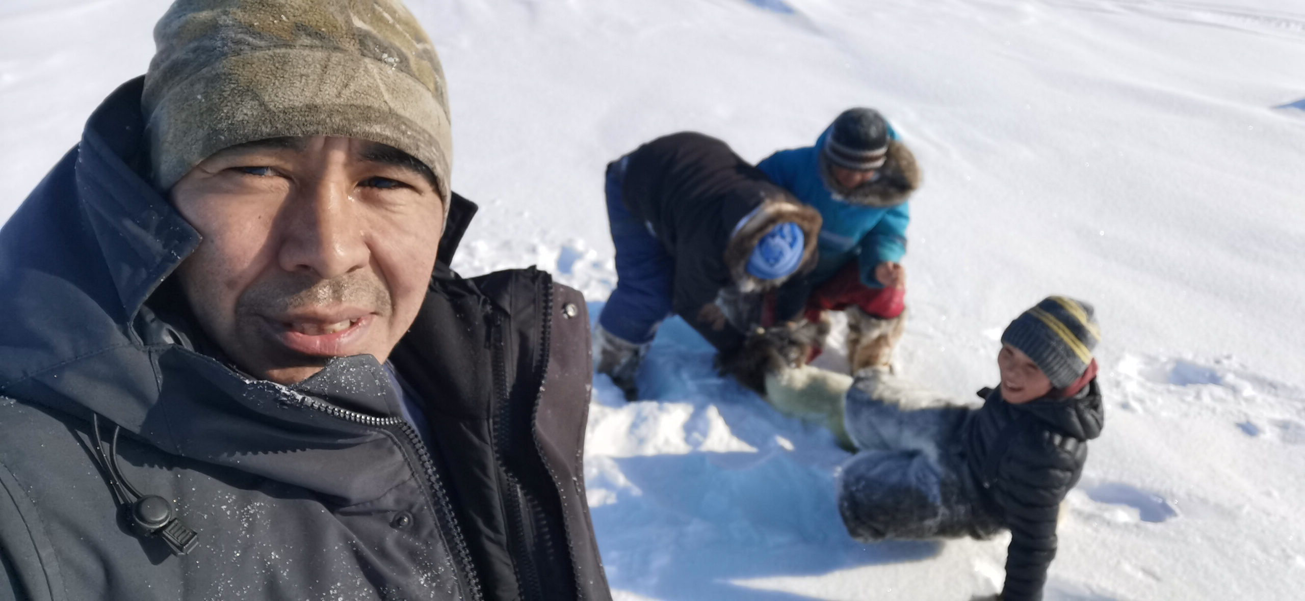 A man standing foreground with children behind him ice fishing