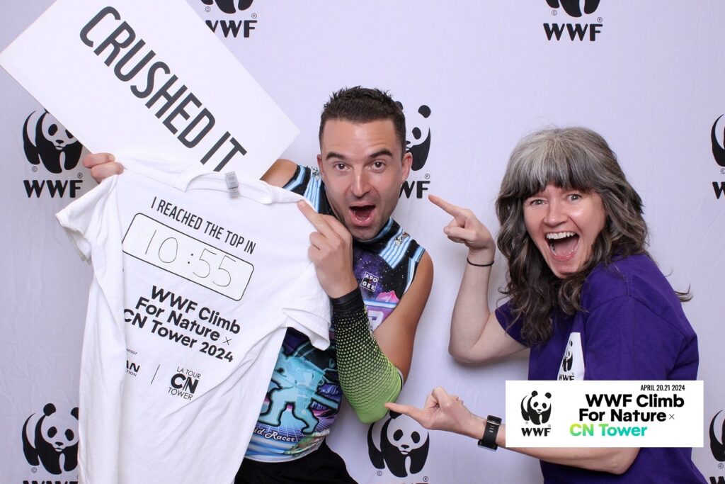 Tyler Kruschenske holds up his T-shirt with 10 minute and 55 second climb time written on the back. Megan Leslie, WWF-Canada's president and CEO celebrates with him. A sign behind them says "Crushed it."