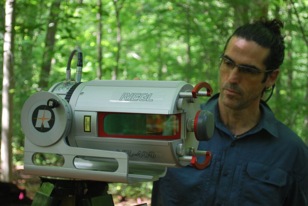 A man standing next to a technical instrument in the woods