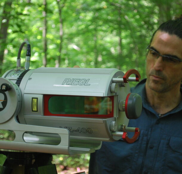 A man standing next to a technical instrument in the woods