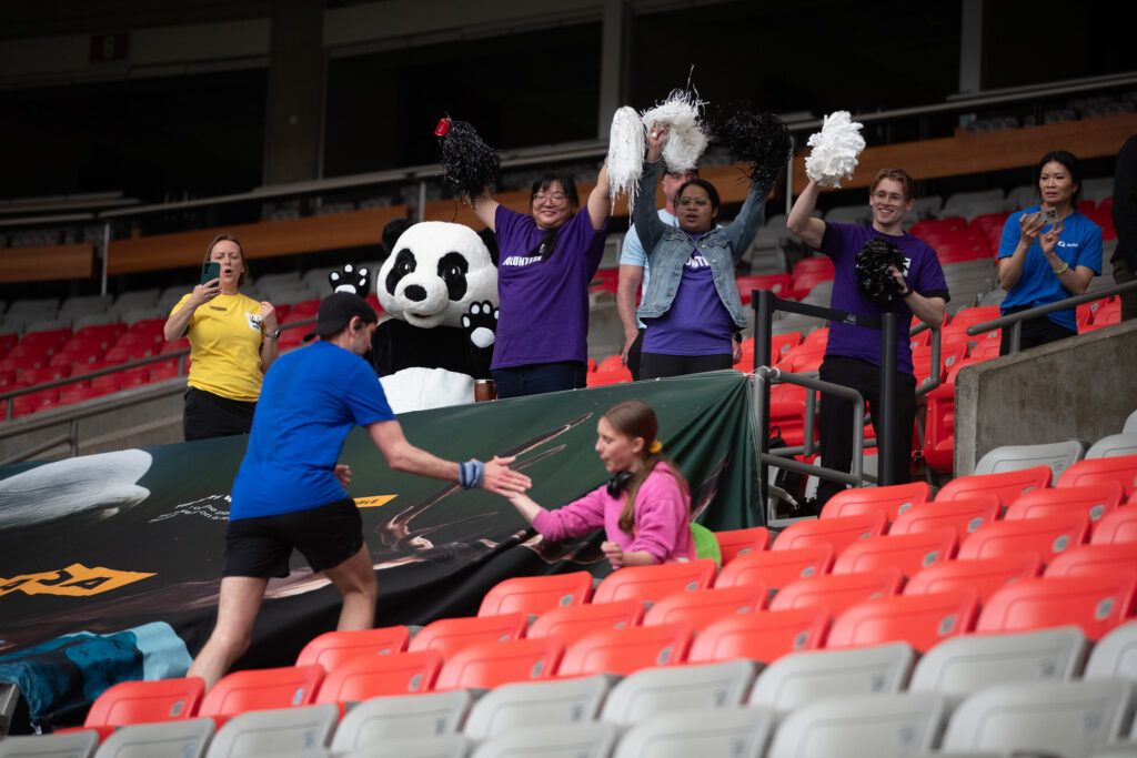 Man in blue t-shirt high fives a young girl in a pink shirt while climbing the stairs at BC Place and being cheered on by WWF staff, volunteers and the panda mascot