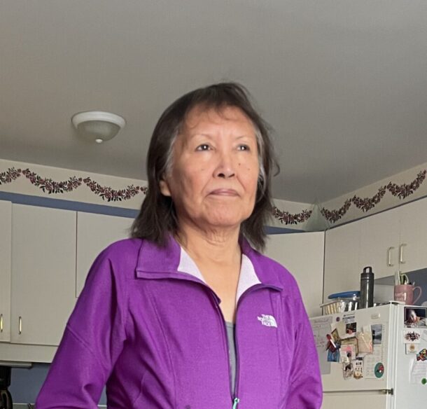 First Nations woman standing in a kitchen wearing a purple fleece jacket