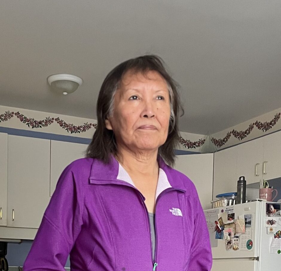 First Nations woman standing in a kitchen wearing a purple fleece jacket