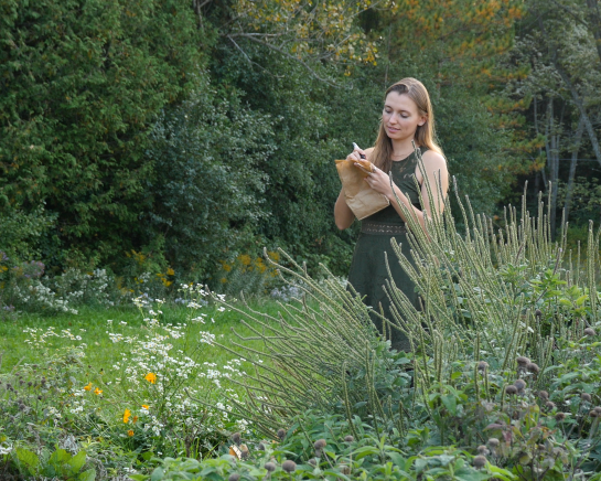Une personne se tient à côté d'un jardin de plantes indigènes et écrit sur un sac en papier.