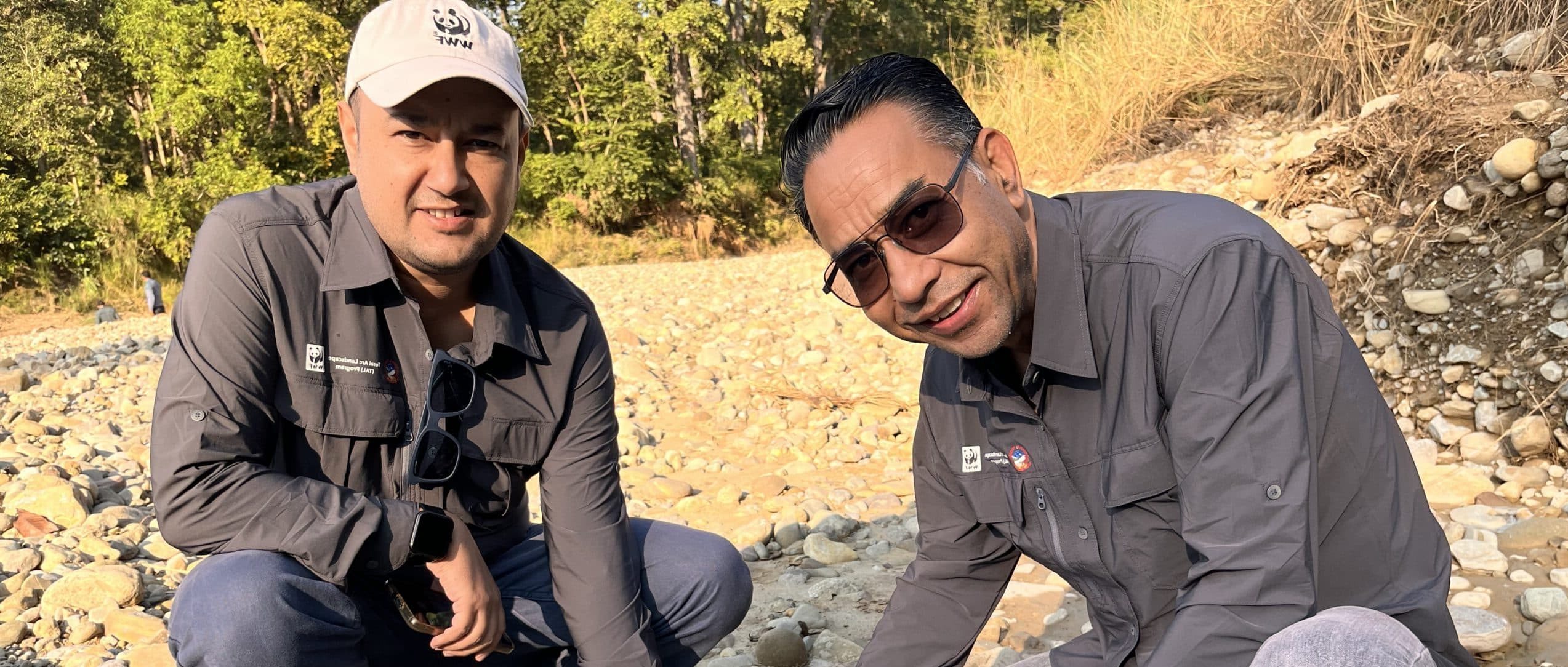 Two men smiling at the camera and pointing at a tiger footprint