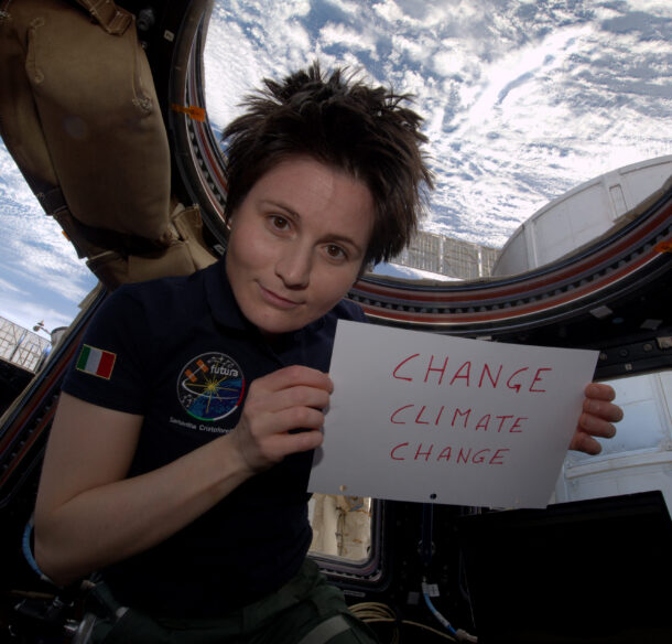 a woman holding a sign that reads change climate change while floating inside a space station