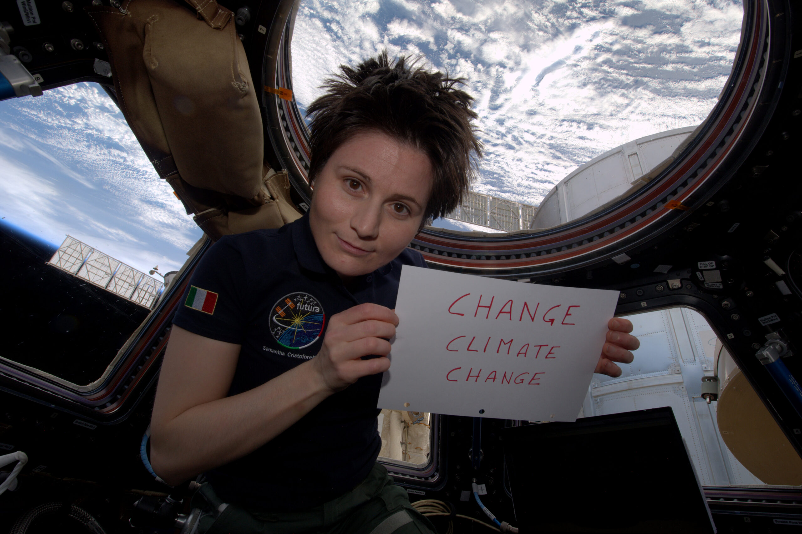 a woman holding a sign that reads change climate change while floating inside a space station