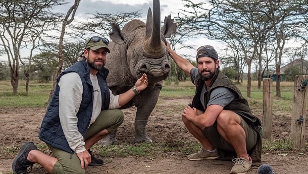 Blake (left) and brother Cody (right) kneeling next to a rhinoceros. 