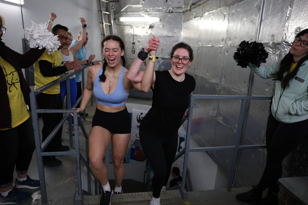 Maya Auchincloss reaching the finish line, holding raised hands with a friend. 