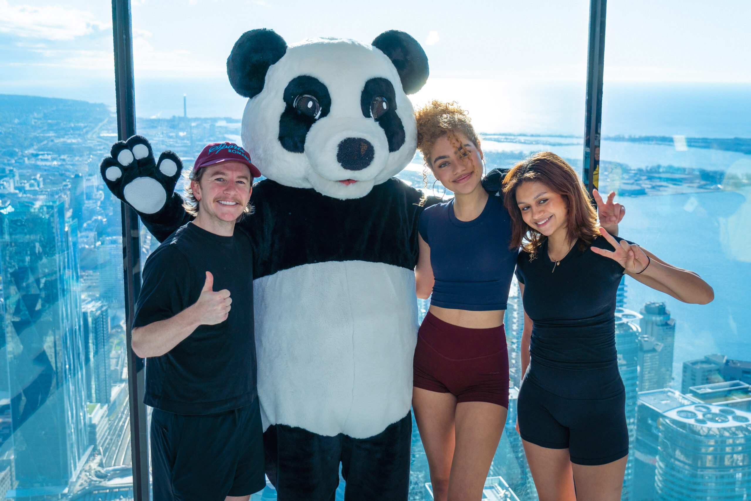 Harrison Browne, Ksenia Kharlamova and Anastasia Kharlamova celebrate at the top of the CN Tower with WWF's panda mascot on May 2.