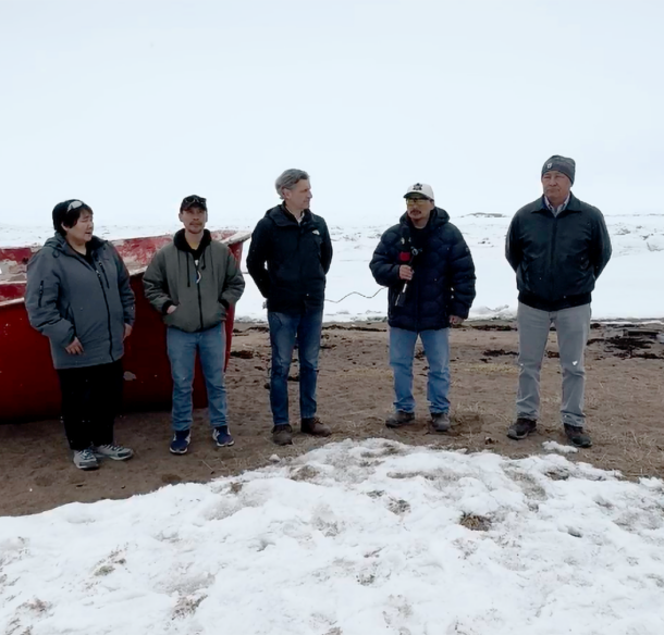 Nunavut community members standing on snow-covered beach beside a boat