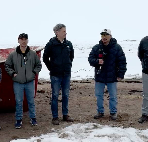 Nunavut community members standing on snow-covered beach beside a boat