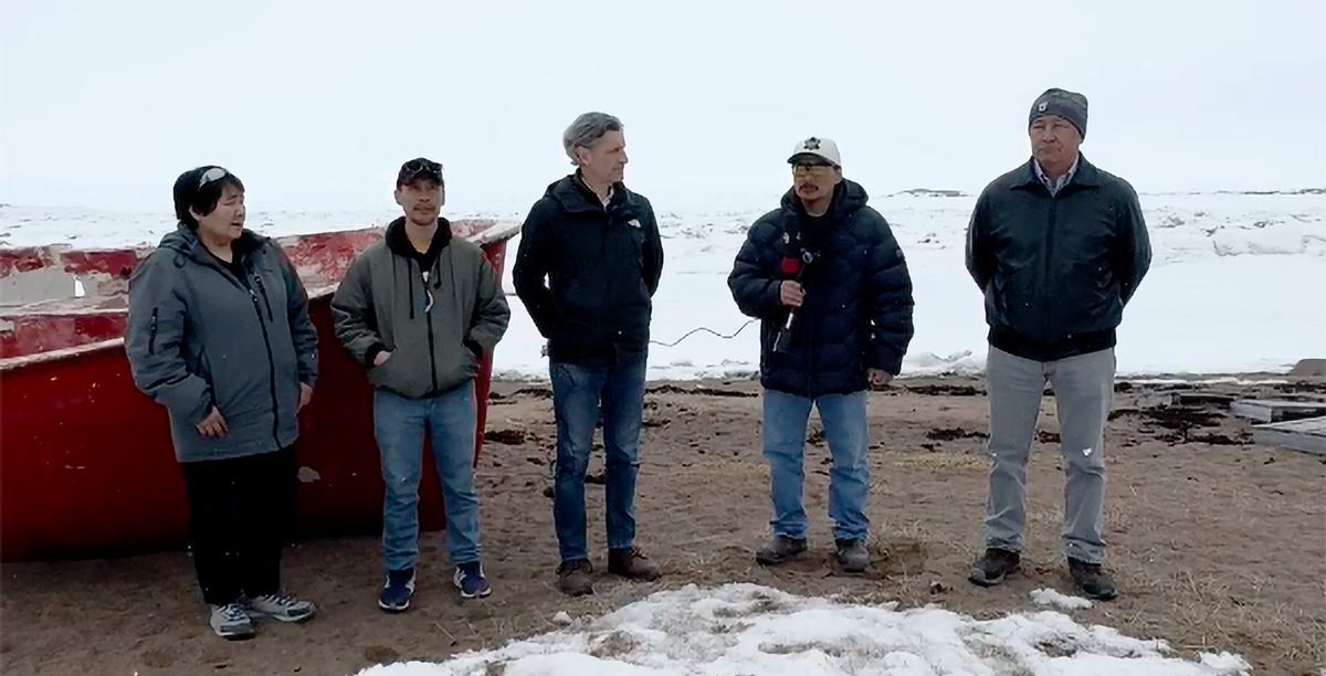 Nunavut community members standing on snow-covered beach beside a boat