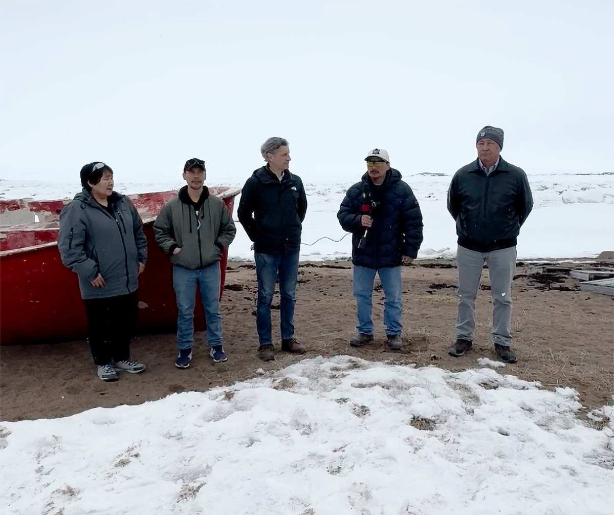Nunavut community members standing on snow-covered beach beside a boat