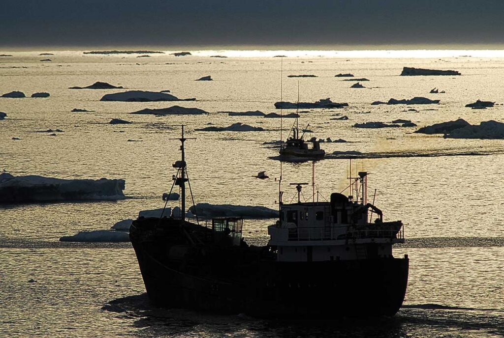 silhouette of ship in water surrounded by small icebergs
