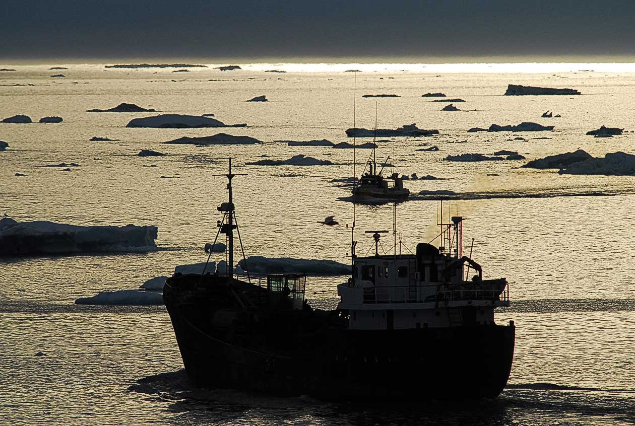silhouette of ship in water surrounded by small icebergs